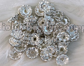 May include: A pile of silver-toned metal bead caps with clear rhinestones. The bead caps are round and have a small hole in the center. The rhinestones are arranged in a circular pattern around the edge of the bead cap.