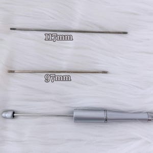 May include: Three silver-toned tools are displayed against a white, fluffy background. Two thin, metal rods, 117mm and 97mm long, are shown. A third tool has a silver handle and a thin metal rod extending from it.