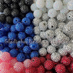 May include: Assortment of colorful rhinestone-covered beads. The beads are in shades of black, white, blue, pink, and red. The beads are all the same size and shape, and they are arranged in a random pattern.