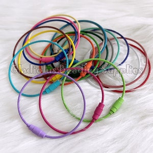 May include: A collection of colorful metal key rings, each with a different color, including red, orange, yellow, green, blue, purple, and white. The key rings are made of braided metal cable and have a metal clasp.