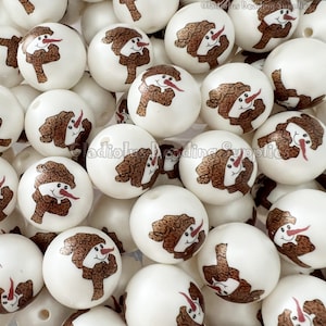 May include: A close-up of a pile of white round beads with a snowman design. The snowman is wearing a brown and white hat and scarf. The beads are approximately 2 cm in diameter.