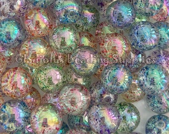 May include: A close-up of a pile of iridescent clear plastic beads with a speckled pattern of glitter in various colors, including pink, blue, green, and purple.