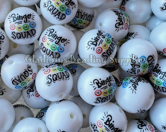 May include: A close-up of white round beads with the text "Bingo Squad" and colourful bingo numbers printed on them.