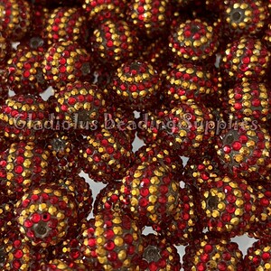 May include: A close-up of a pile of red and gold round beads. The beads are covered in small, sparkling rhinestones.