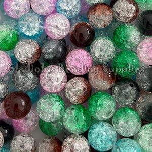 May include: A collection of colorful, crackle-effect glass beads in various colors, including pink, green, blue, brown, black, and silver. The beads are round and have a textured surface. The text "Gladiolus Beading Supplies" is visible.