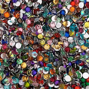 May include: A large assortment of colorful round rhinestones with silver settings. The rhinestones are scattered on a white surface.