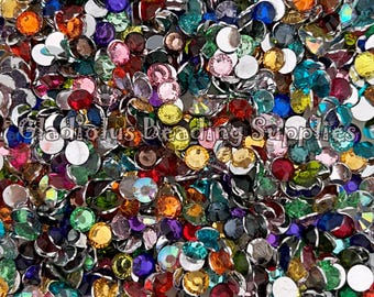 May include: A large assortment of colorful round rhinestones with silver settings. The rhinestones are scattered on a white surface.