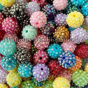 May include: A close-up image of a variety of colorful, iridescent, round, plastic beads. The beads are covered in small, sparkly rhinestones.