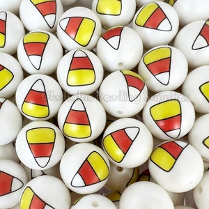 May include: A close-up of a group of white round beads with a candy corn design. The beads are yellow, orange, and white.