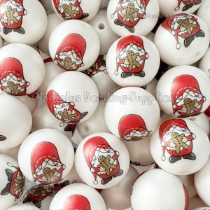 May include: A close-up of a pile of white wooden beads with a red and white Santa Claus design holding a gingerbread man. The beads are for crafting and making jewelry.