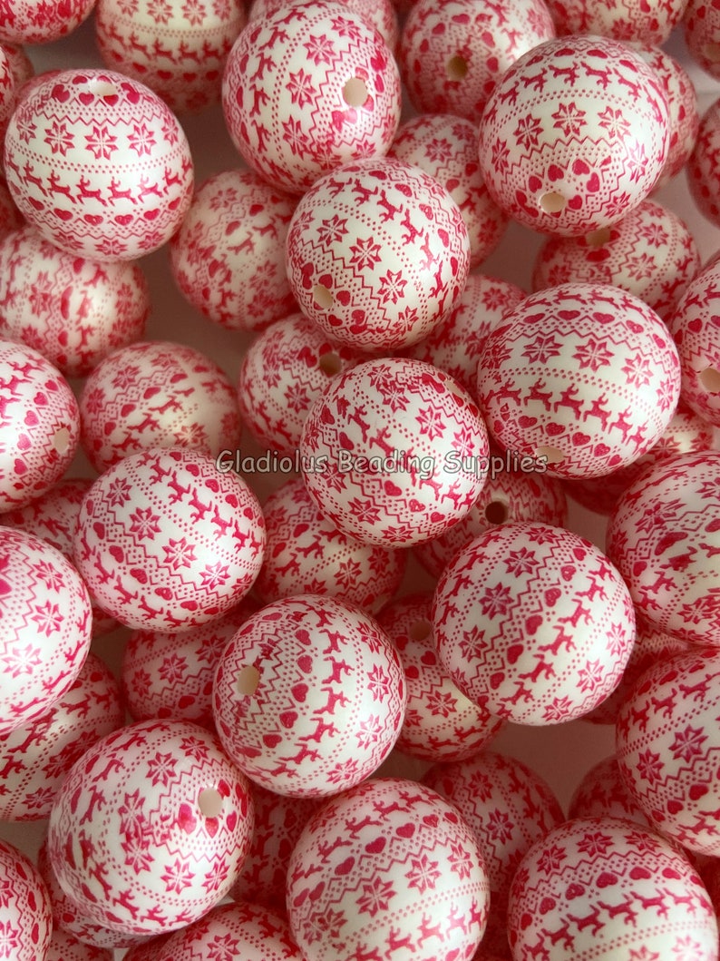 May include: A close-up of a pile of large, white, round, silicone beads with a red and white snowflake pattern. The beads are perfect for making necklaces, bracelets, and other jewelry.