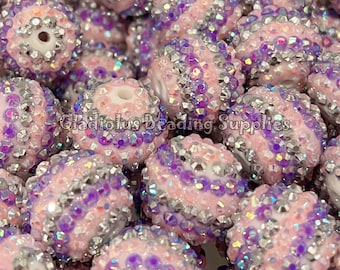 May include: A close-up of a pile of pink and purple round beads with silver glitter. The beads are all the same size and have a smooth, shiny finish.