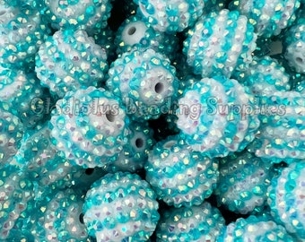 May include: A close-up of a pile of turquoise and white round beads. The beads are covered in iridescent rhinestones.