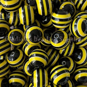 May include: A close-up of a group of black and yellow striped round beads. The beads are glossy and have a smooth finish.