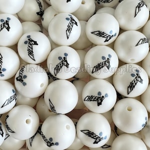 May include: A large group of white round beads with the word "CHEERS" printed in black on each bead. The beads have a slight pearlescent sheen.
