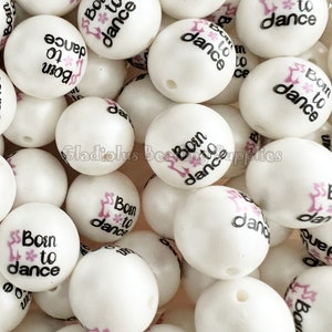 May include: A close-up of a pile of white silicone beads with the text "Born to Dance" and a pink dancing shoe graphic printed on each bead.