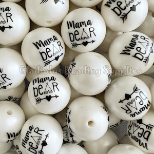 May include: A close-up of a pile of white silicone beads with black text that reads "Mama Bear" and a small tent graphic. Each bead has a black arrow and heart graphic.