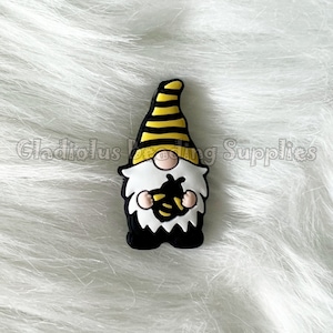 May include: A black and yellow gnome figurine holding a bee. The gnome is wearing a yellow and black striped hat.