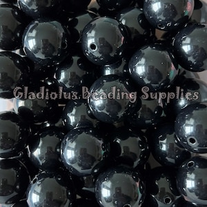 May include: A pile of glossy, black beads with a hole drilled through each. The beads are spherical and reflect light, creating highlights. The text "Gladiolus, Beading Supplies" is visible at the bottom of the image.