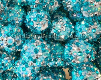 May include: Close-up of a pile of turquoise blue and silver round beads. The beads are covered in small, sparkly rhinestones.