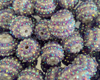 May include: A close-up of a group of white, iridescent, round beads with a hole in the center. The beads are covered in small, sparkly rhinestones.