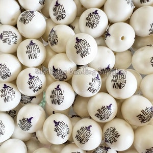 May include: A close-up of a pile of white, round beads with a black witch hat and the text "Witch Way to the Wine?" printed on them.
