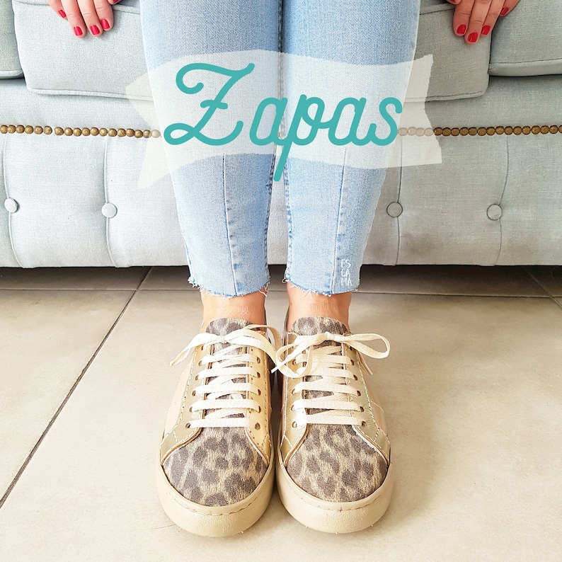 May include: A pair of gold and leopard print sneakers with white laces. The sneakers are worn by a person wearing blue jeans. The word "Zapas" is written in a white banner above the sneakers.