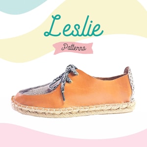 Op de afbeelding: Een bruine leren espadrille met een zwarte en witte gepatroneerde neus. De schoen heeft een touwzool en veters. De tekst "Leslie Patterns" is zichtbaar in de afbeelding.