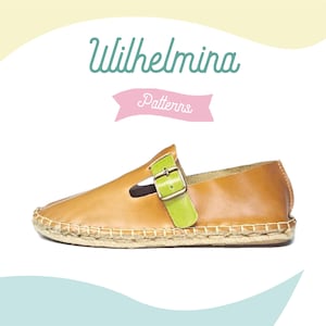 May include: A tan leather espadrille shoe with a green strap and buckle. The shoe has a woven sole and is labeled "Wilhelmina Patterns". The design features a classic, casual style.