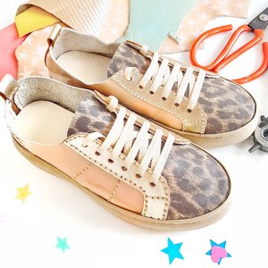 May include: A pair of low-top sneakers with a leopard print design. The sneakers are made of leather and have a cream-colored sole. The laces are white.