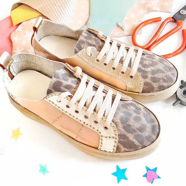 May include: A pair of low-top sneakers with a leopard print design. The sneakers are made of leather and have a cream-colored sole. The laces are white.