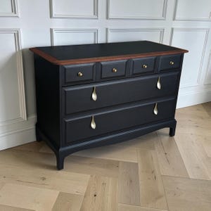 May include: A black wooden chest of drawers featuring a dark wood top surface, four small upper drawers with round gold knobs, and two large lower drawers fitted with elongated gold leaf-shaped handles, all supported by four short, sturdy legs.
