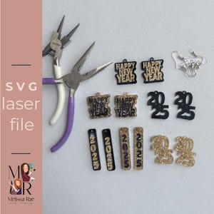 May include: A set of laser cut earrings and charms featuring a New Year's theme. The earrings are black with gold glitter and say "Happy New Year". The charms are black with gold glitter and say "2023" and "Happy New Year".