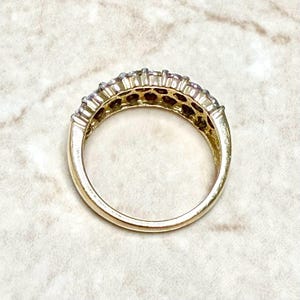 May include: A gold band ring with a row of small, clear stones set in a channel setting.