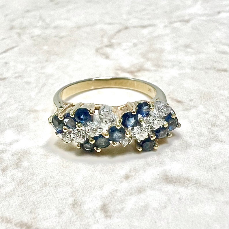 May include: A gold band ring with a cluster of blue sapphires and white diamonds set in a wave-like pattern.
