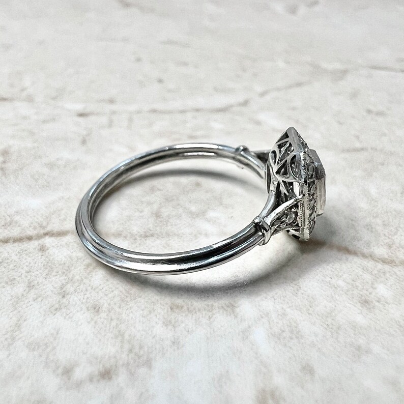 Puede incluir: Un anillo de plata con una piedra central de forma cuadrada rodeada por un delicado dise&ntilde;o de filigrana.