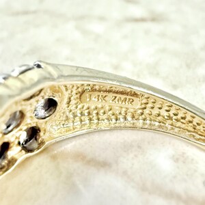 May include: Close-up of the inside of a gold ring with the inscription "14K ZMR" on the band.
