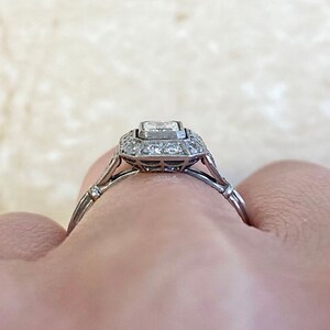 Puede incluir: Un anillo de compromiso de plata con un diamante central de forma cuadrada rodeado por un halo de diamantes m&aacute;s peque&ntilde;os. El anillo tiene una banda delicada con un detalle de milgrain.
