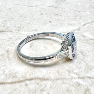 May include: A silver ring with a square-shaped blue gemstone surrounded by smaller diamonds. The ring is engraved with the text "P1900".