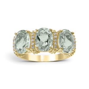 May include: A yellow gold ring featuring three oval-cut light green gemstones arranged horizontally. The central stone is flanked by two smaller oval stones, with small clear accent stones set along the vertical prongs between each main gemstone.