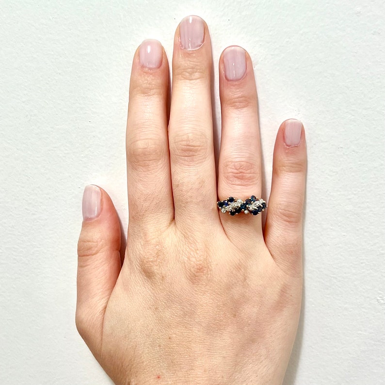 May include: A gold ring with a cluster of blue and white gemstones. The ring is set on a white background.