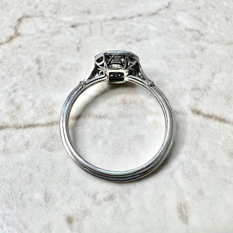 Puede incluir: Un anillo de compromiso de plata con un diamante de forma cuadrada engastado en un dise&ntilde;o delicado e intrincado. El anillo tiene una banda simple con un perfil ligeramente redondeado.