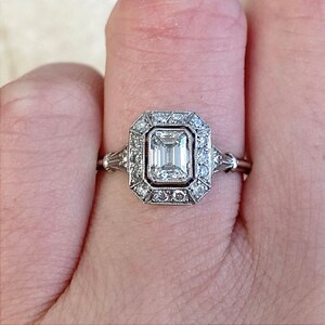 Puede incluir: Un anillo de compromiso de plata con un diamante cuadrado de talla esmeralda rodeado por un halo de diamantes m&aacute;s peque&ntilde;os.