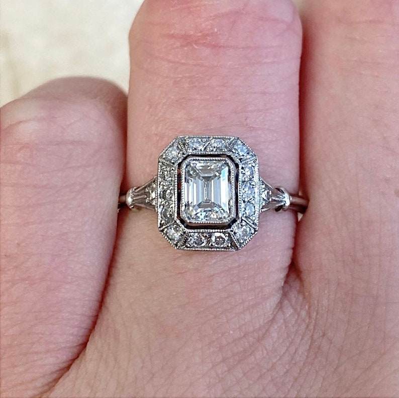 Puede incluir: Un anillo de compromiso de plata con un diamante cuadrado de talla esmeralda rodeado por un halo de diamantes m&aacute;s peque&ntilde;os.
