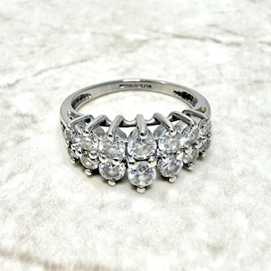 Puede incluir: Un anillo de plata con una fila de piedras redondas transparentes. El anillo está engastado con varias piedras en un patrón graduado.