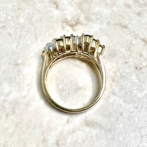 May include: A gold ring with a row of oval-shaped blue and clear gemstones.