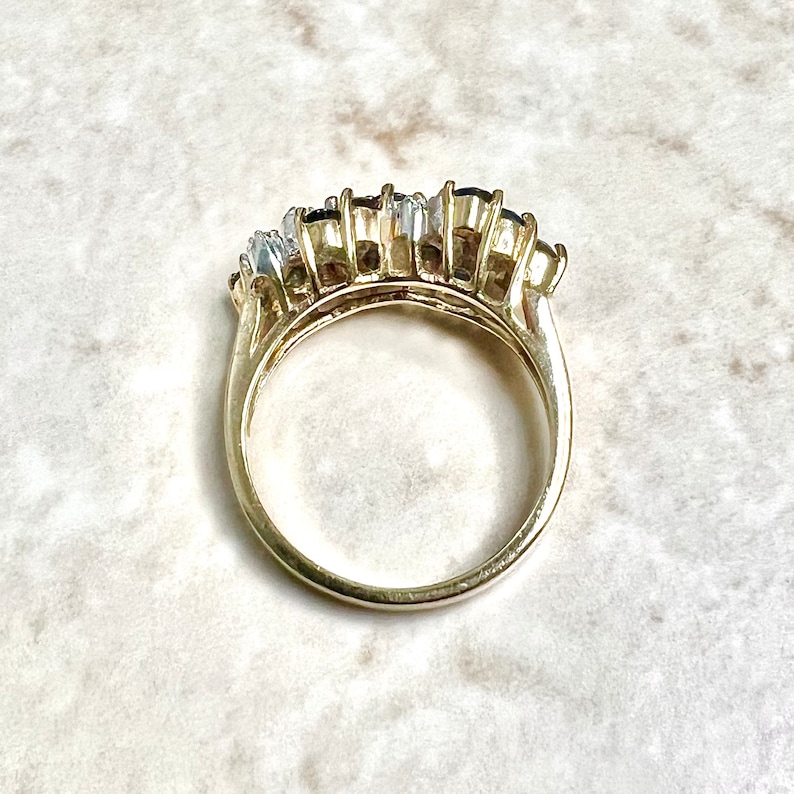 May include: A gold ring with a row of oval-shaped blue and clear gemstones.