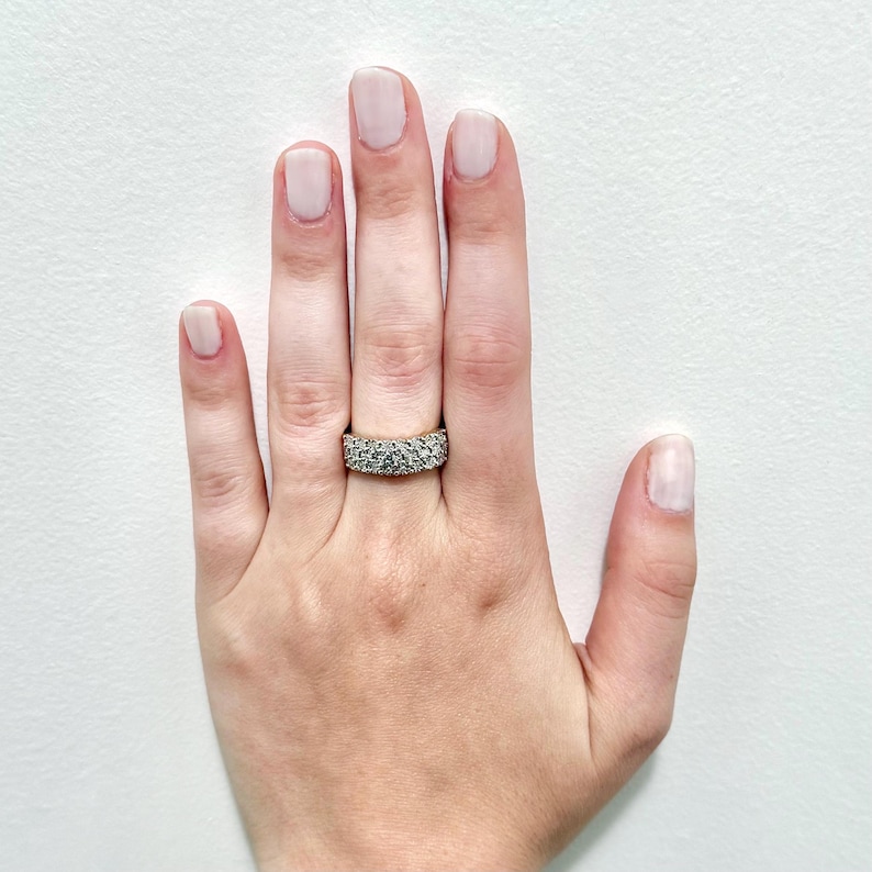 May include: A hand wearing a gold band ring with a row of small, clear stones.