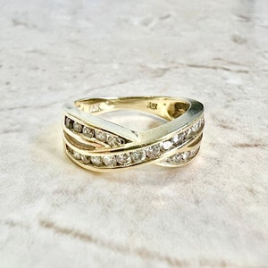 May include: A gold band ring with a criss-cross design featuring a row of small diamonds on each band.