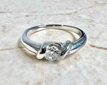 Könnte beinhalten: Ein silberner Ring mit einem einzelnen runden Diamanten, der in einem verdrehten Band gefasst ist.